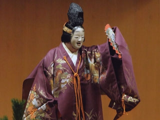 Intérprete de Noh en la obra Matsukaze, llevando un kimono violeta, máscara noh y un abanico
