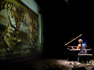 Yoko Suzuki tocando el piano ante una imagen de un tigre