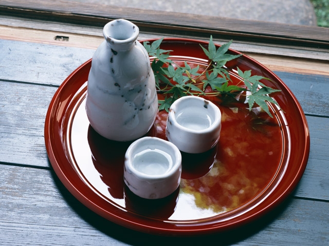 Botella tokkuri y vasos ochoko de saje sobre una bandeja decorada con una hoja verde