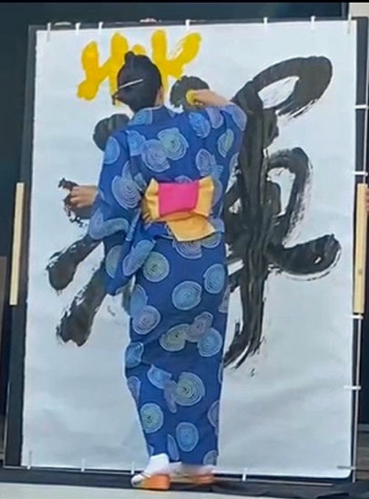 Satomi Tanaka creando una obra de caligrafía sumie de gran formato en un kimono azul