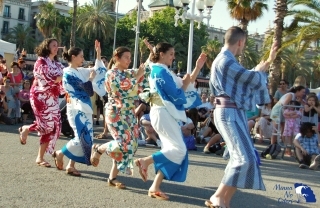 Varios miembros de Minna no odori vestidos en yukata y bailando en la calle ante unas palmeras